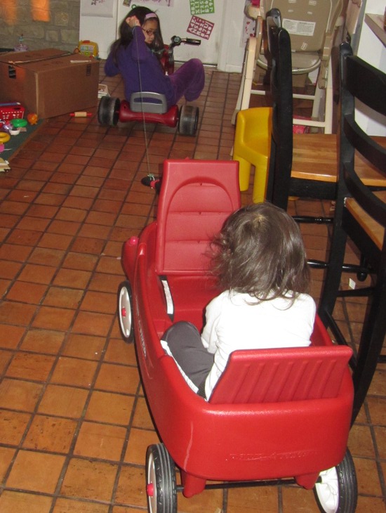 Yaya rides the tricycle and tows Adik in the red wagon